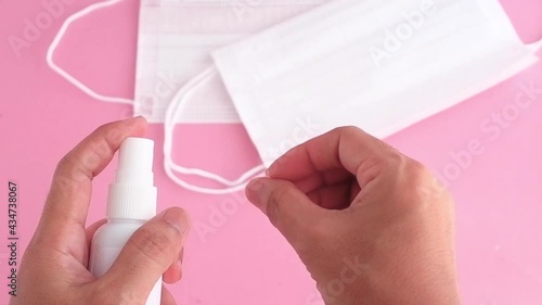 hands holding bottle alcohol sanitizer spraying with facemask on pink background, pandemic prevention Coronavirus, Covid-19