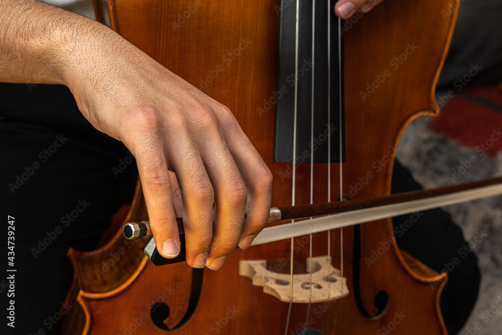 Selective focus of a teenager practicing with the cello musical instrument using the bow to pluck the strings during a lesson. Selective focus of a teenager practicing with the cello musical instrument using the bow to pluck the strings during a lesson.
