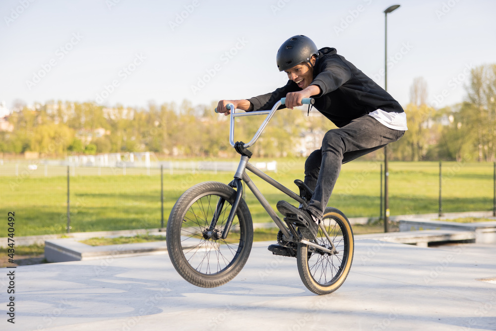 Crazy biker rides his low bike at the skatepark, bmx lifting the front wheel and being in the air he twists his body, hips, performs tricks, laughs, smiles