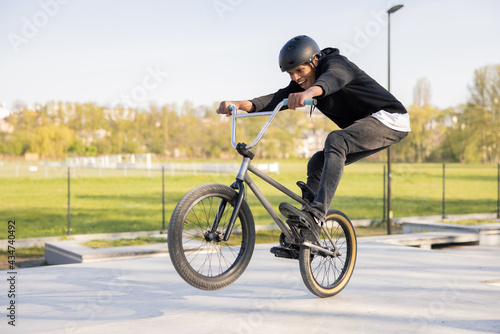 Crazy biker rides his low bike at the skatepark, bmx lifting the front wheel and being in the air he twists his body, hips, performs tricks, laughs, smiles