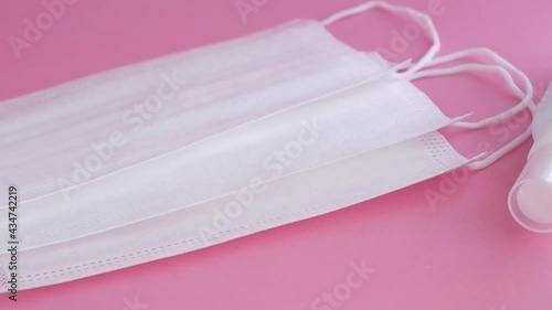 disposable masks, earloop type, with spray alcohol bottle on soft pink surface, slowly movement