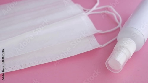 disposable masks, earloop type, with spray alcohol bottle on soft pink surface, slowly movement