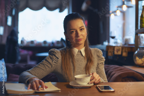 Beautiful woman sitting in a cafe at a table drinking tea and making notes in a notebook