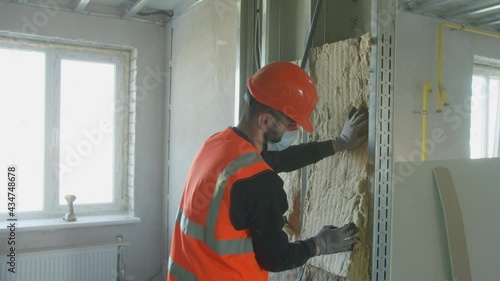 Male builder in mask putting foam into drywall