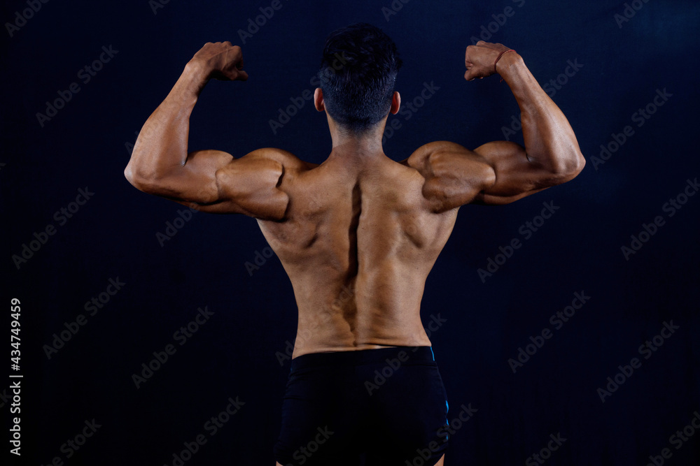 Muscular bodybuilder male in gym. Black background. Back profile.Showing arm and back muscles.