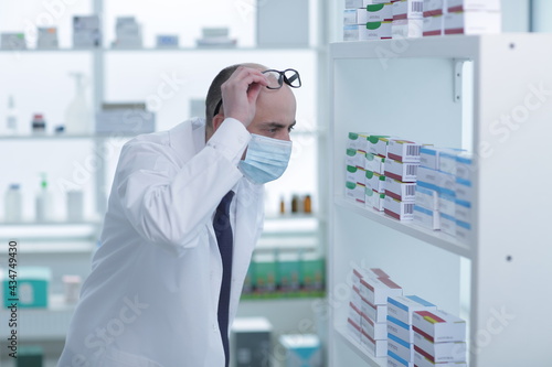 Man pharmacist in protective face mask working in drugstore
