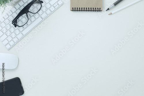 White keyboard mouse glasses pen pencil notepad phone flower in a pot on white background