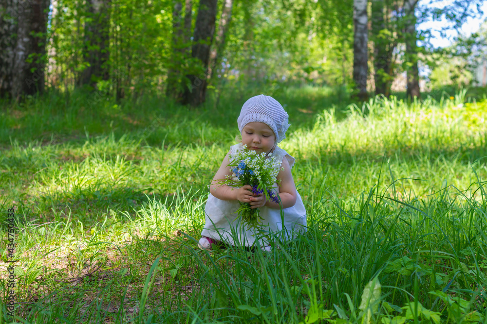 Cute baby girl in white dress and panama hat in summer holds a bouquet of delicate wildflowers in the forest Cute baby girl in white dress and panama hat in summer holds a bouquet of delicate wildflowers in the forest