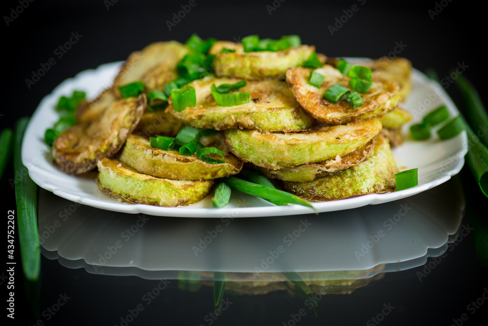 fried zucchini in circles with fresh herbs in a plate on a black