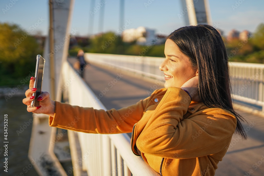 Obraz premium Beautiful woman standing on bridge and making selfie