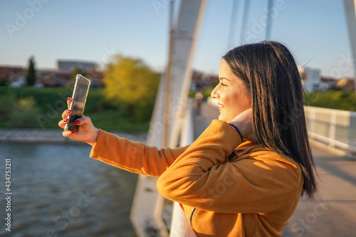 Beautiful woman standing on bridge and making selfie
