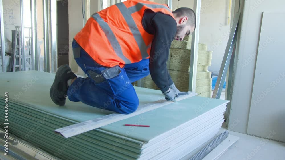 Male builder measuring and cutting gypsum panel Male builder measuring and cutting gypsum panel