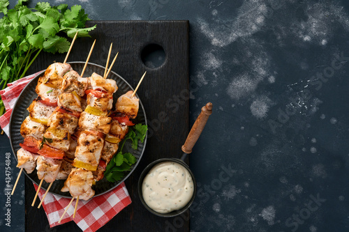 Chicken shish kebab or skewers kebab on wooden board, spices, herbs and vegetables on dark grey background. Barbecue Raw ingredients for goulash or shish kebab. Top view. Free copy space.
