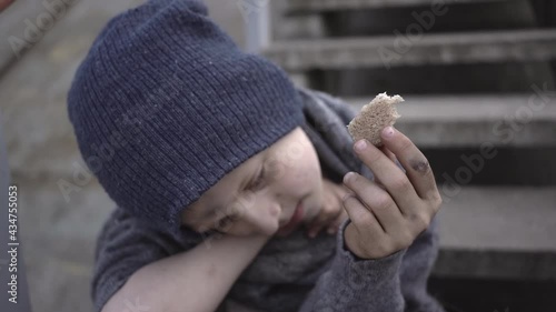 homeless boy sits on stairs in bandoned place holding bread in his hand migration homeless child with a dirty face and hands needs help Social problems custody Homeless people refugee escape from war photo