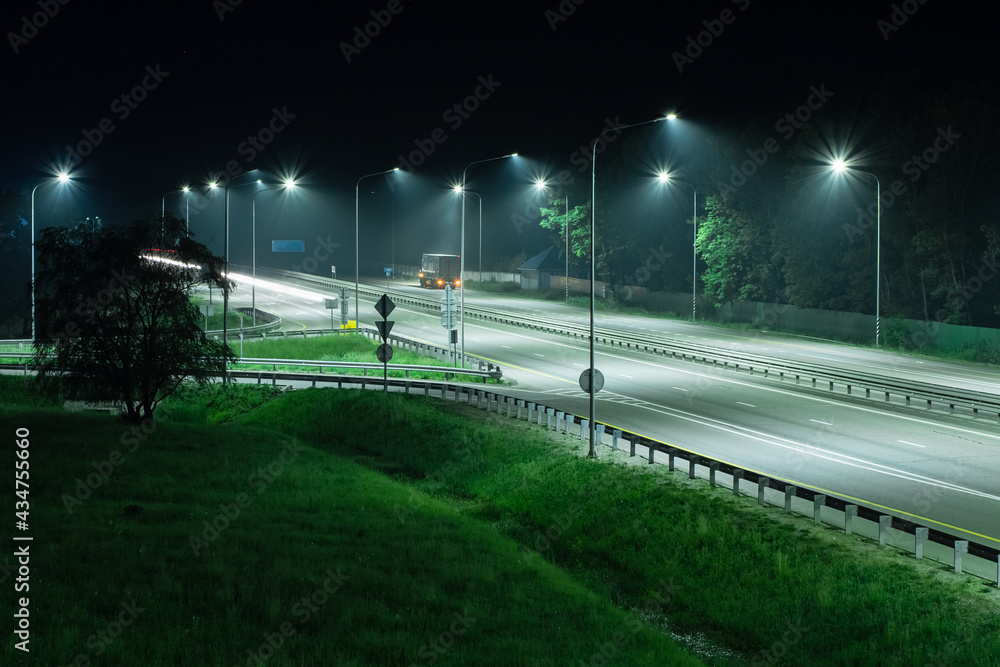 Night highway in the light of streetlights. A truck is parked on the side of the road Night highway in the light of streetlights. A truck is parked on the side of the road