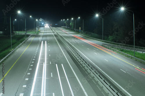 Country night track lit by lanterns. It shows streaks of light from the headlights of passing cars