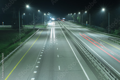 A country highway at night  lit by streetlights and long streaks of light from the headlights of passing cars