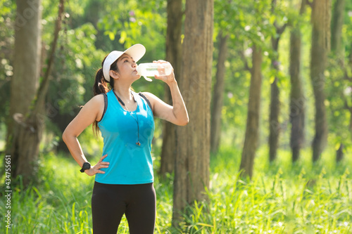 Healthy athletic woman drinking pure water after go running to be fresh in the nature park. Asian runner woman after exercise. Healthy and Lifestyle concept. On Nature background .