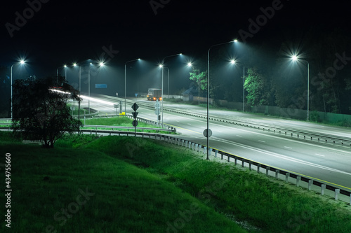 Night highway in the light of streetlights. A truck is parked on the side of the road © VeNN