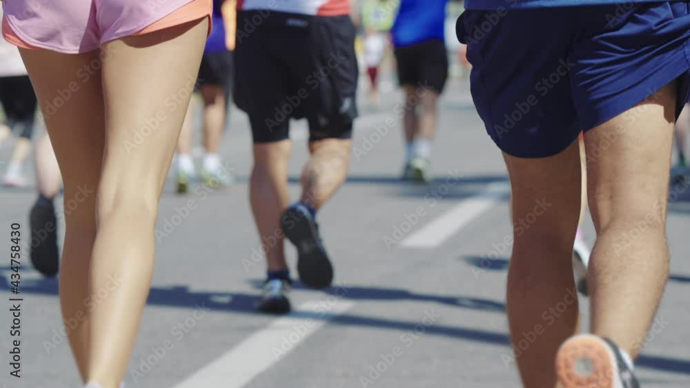 Buttocks of athletes competing in marathon in slow motion, crowd of people running in front of him. Partial view from behind of fit couple taking part in sports event. Gender equality Buttocks of athletes competing in marathon in slow motion, crowd of people running in front of him. Partial view from behind of fit couple taking part in sports event. Gender equality