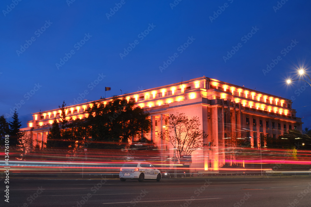 Victory Palace (Palatul Victoria) in Bucharest houses the Prime Minister of Romania and his cabinet - evening with car trails, street lights, police car.