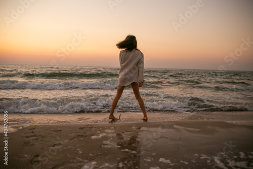 A slender girl in white clothes runs along the beach against the background of the sea. A sports girl runs along the embankment of the sea. Healthy woman on the beach