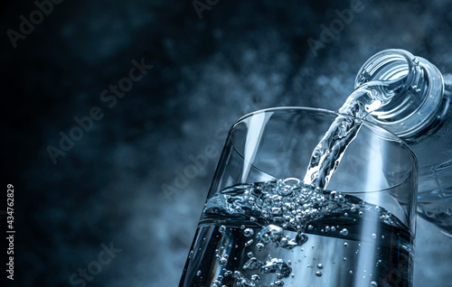 Pouring water from bottle into glass on black background photo