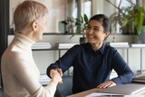 Overjoyed young Indian businesswoman shake hand of female colleague get acquainted greeting at business meeting. Happy multiracial women employees handshake close deal or make agreement in office.