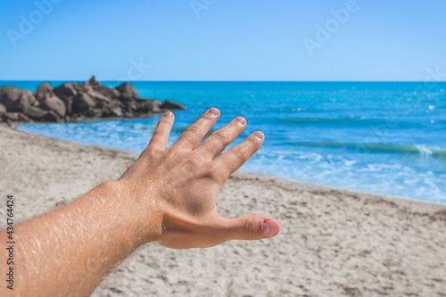 The young man stretched his hand forward to the sea and sky on the beach. The concept of freedom and rest at sea