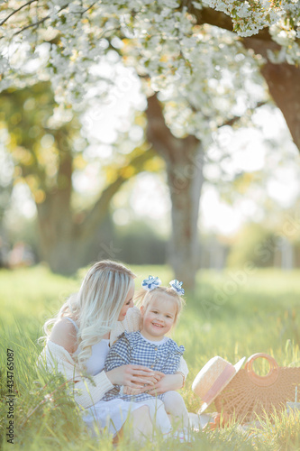A beautiful young mother with her little daughter are resting on a picnic in the flowering garden. White flowers. Spring. Happiness.