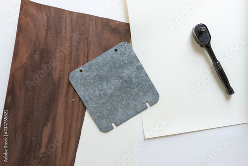 galvanized metal plate with holes, sprocket wrench, paper, and wood veneer - photographed from above with ambient light