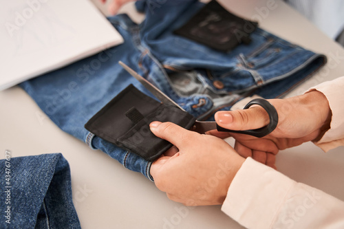 Woman hands cutting fabric with scissors at the table with jeans at the background