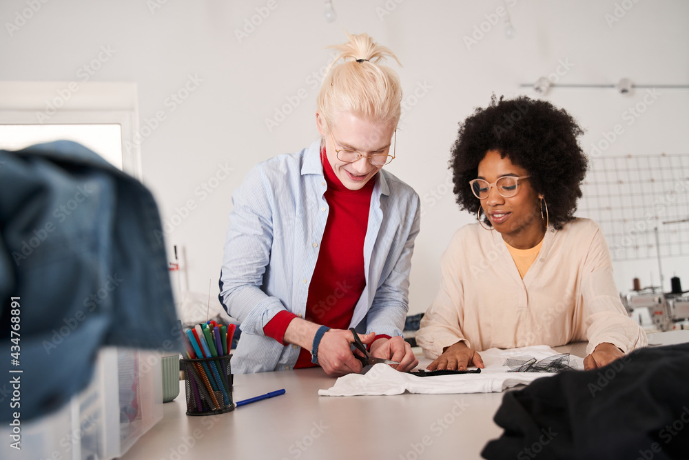 Woman looking attentively at the t shirt and listening ideas from her colleague Woman looking attentively at the t shirt and listening ideas from her colleague