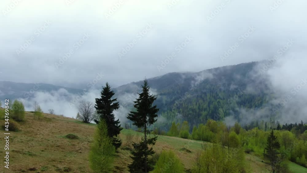 Drone flying through morning fog in spring mountains. Aerial view of mist, cloud and fog hanging over a wood forest after a rain Drone flying through morning fog in spring mountains. Aerial view of mist, cloud and fog hanging over a wood forest after a rain