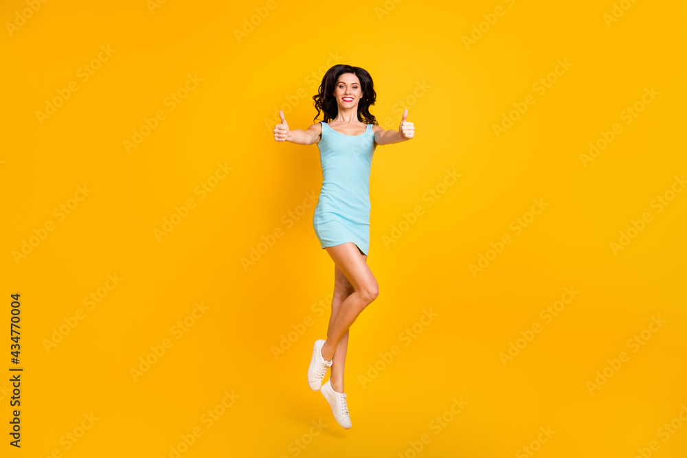 Photo of positive lady jump raise two thumbs up wear blue short dress sneakers isolated yellow color background Photo of positive lady jump raise two thumbs up wear blue short dress sneakers isolated yellow color background