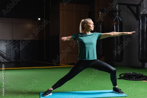 amputee woman standing in warrior pose on fitness mat