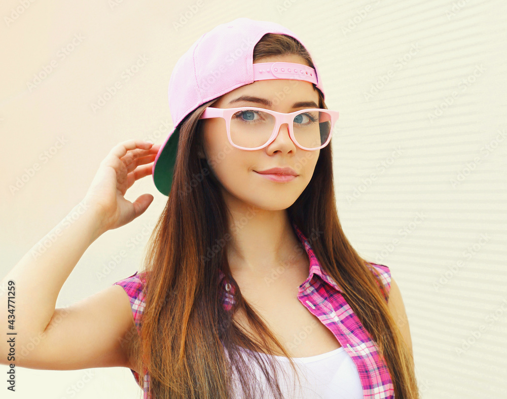 Portrait of young woman wearing a pink baseball cap and glasses in a city on a white background