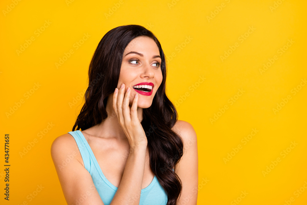 Photo of flirty charming girl look empty space hand cheek wear blue top isolated yellow color background Photo of flirty charming girl look empty space hand cheek wear blue top isolated yellow color background