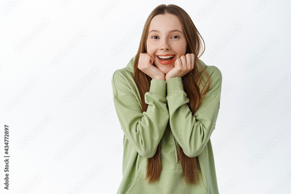Smiling teenage girl lean on hands and look at something adorable, look fascinated and amused, checking out something beautiful, standing over white background Smiling teenage girl lean on hands and look at something adorable, look fascinated and amused, checking out something beautiful, standing over white background