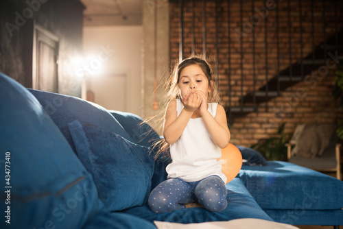 Girl sitting at the sofa and blowing greeting balloons for her mother