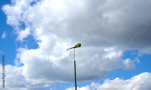 A sign in the form of an arrow showing the direction of the wind against a background of blue sky and white clouds. Bright sunny day