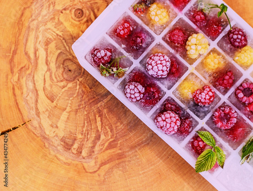 Ice cubes with raspberries. Ice tray with berries on wood background. Top view.
