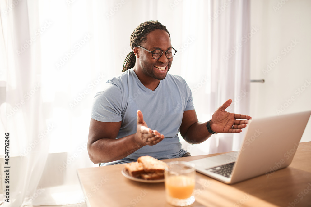 Handsome young multiracial man with dreadlocks working with laptop at the kitchen