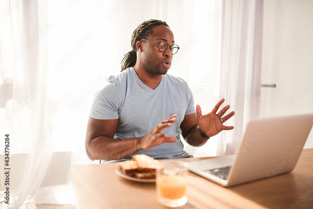 Bearded man smiling and looking at the laptop screen while working at the kitchen Bearded man smiling and looking at the laptop screen while working at the kitchen