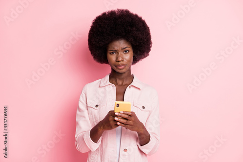 Portrait of lovely disappointed wavy-haired girl using gadget dislike post smm isolated over pink pastel color background