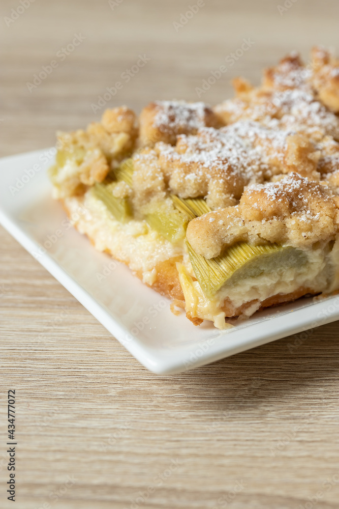 Kuchen mit Rhabarber und Streusel aus einem Blech auf einem Tisch aus hellem Holz Kuchen mit Rhabarber und Streusel aus einem Blech auf einem Tisch aus hellem Holz