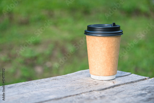 Close-up paper cup of coffee on natural background on a wooden bench. For a coffee shop