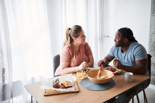 Man talking with his wife while sitting at the table and eating salad