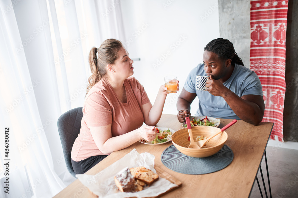 Couple talking during breakfast while sitting at the kitchen and eating salad