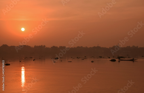 Sunrise over the river with a fisher boat passing by. Red sun reflection on the river of Ganga in the morning